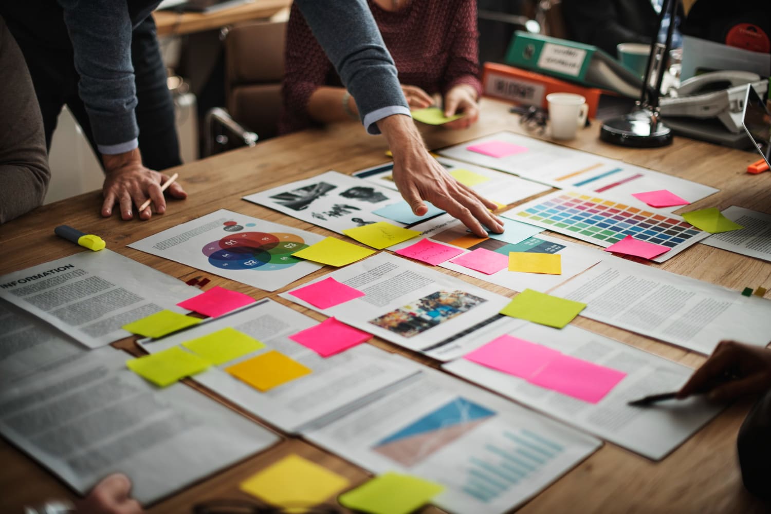 Team collaborating around a table covered with sticky notes, charts, and design documents